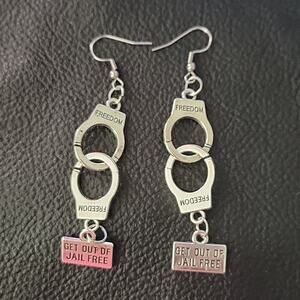 Handcuff earrings inscribed with freedom and a Get out of jail free charm
